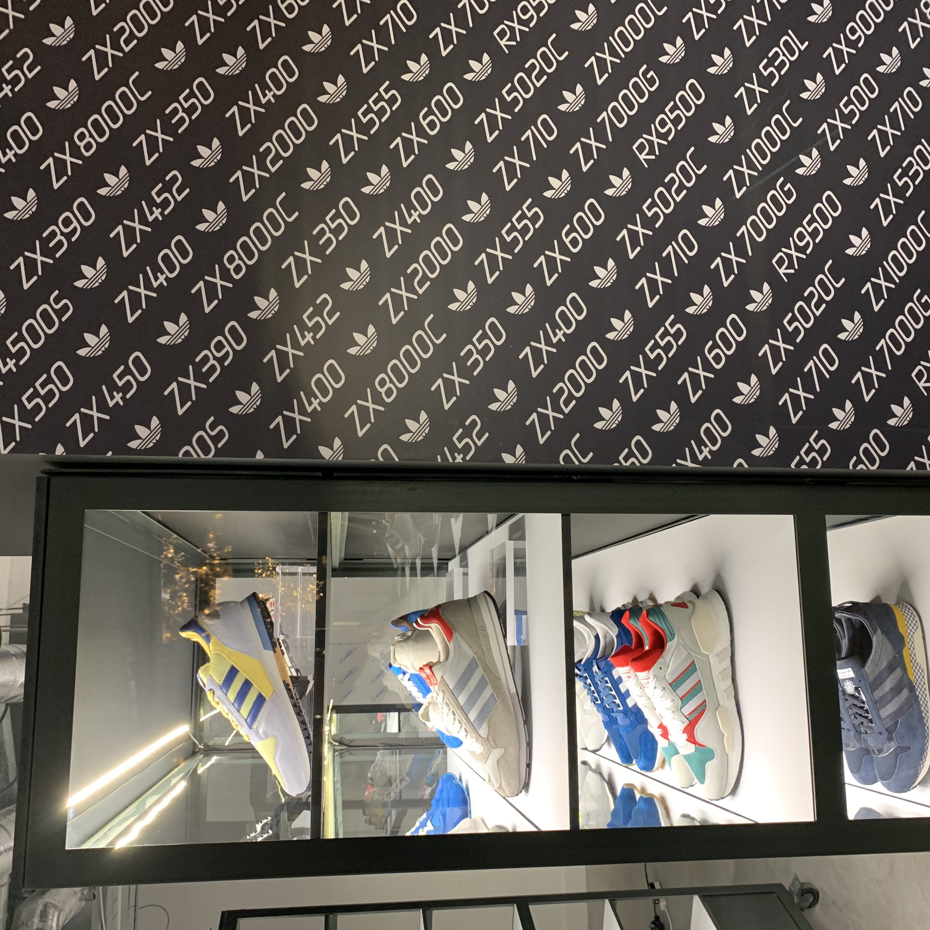 Adidas retail display with ZX model-name patterned wall graphic above illuminated trainer cases