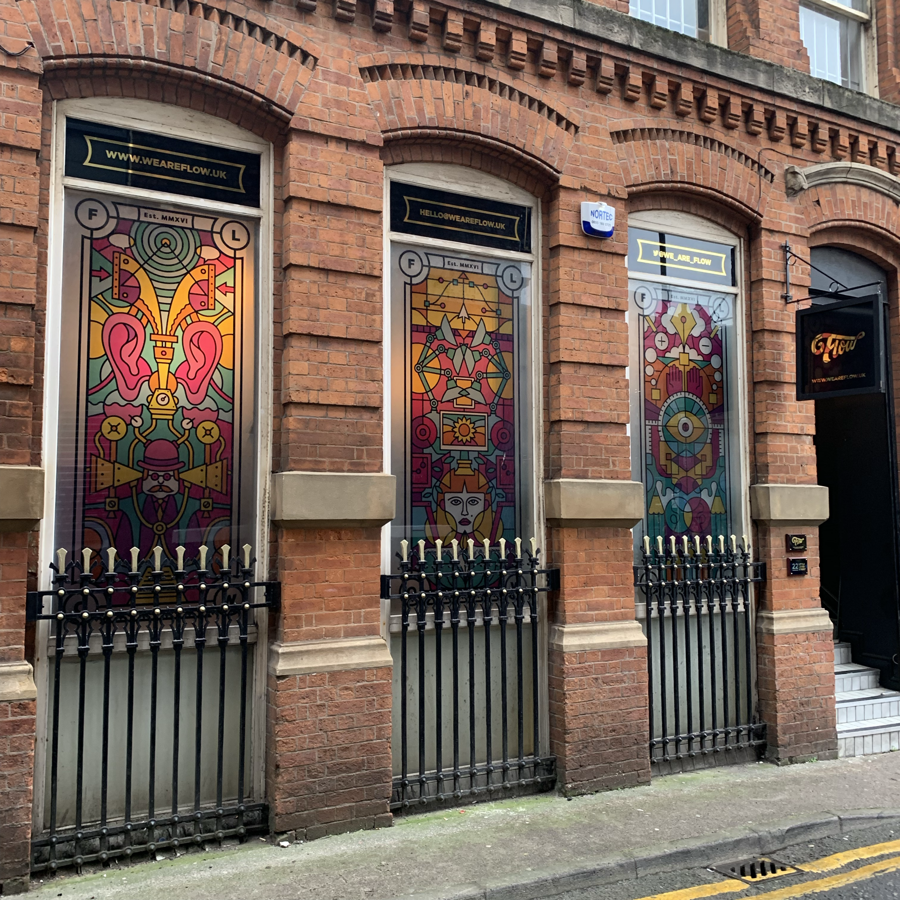 Flow's brick frontage with three tall stained-glass-style printed window panels in vivid pink, yellow and teal