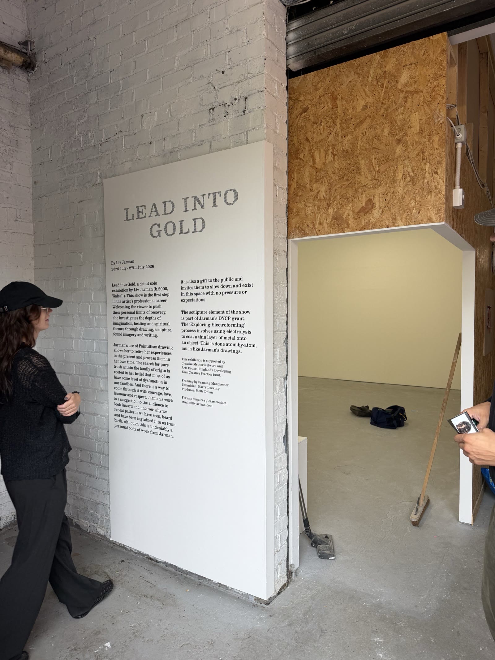 Cut-vinyl gallery wall text reading Lead Into Gold for Liv Jarman's exhibition, applied to a white brick gallery wall