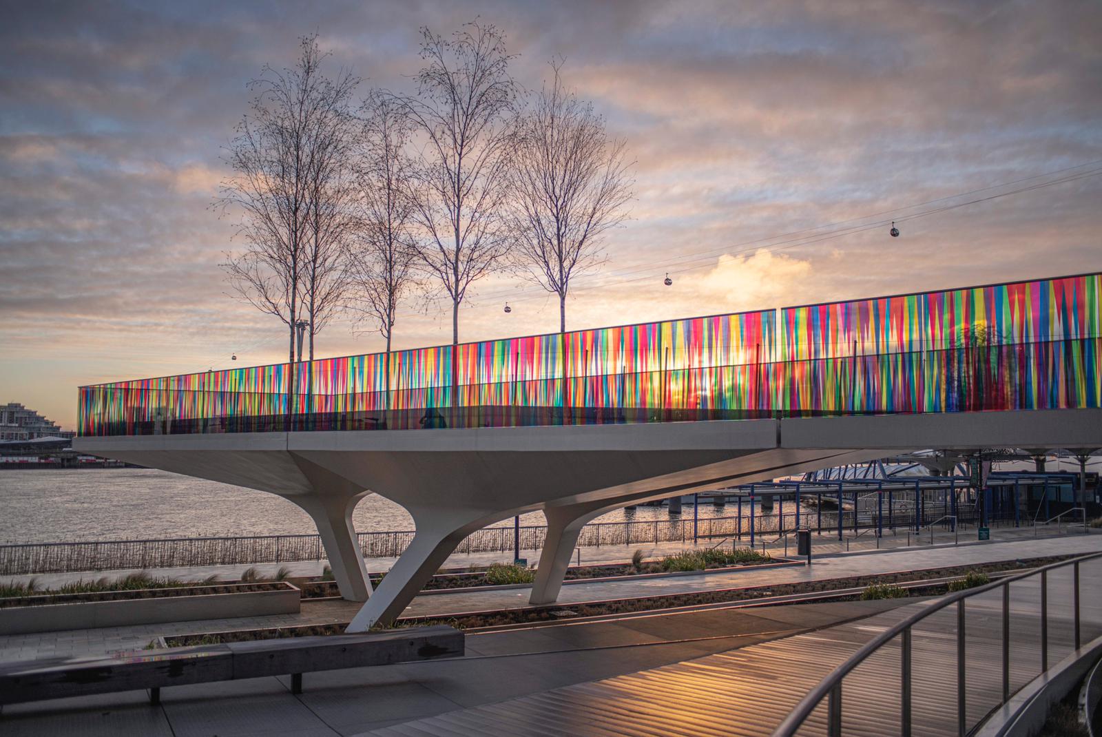 Liz West colour installation cladding a riverside bridge in translucent multicoloured strips at sunset