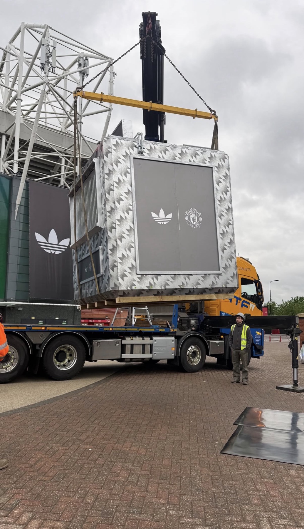 Adidas x Manchester United branded modular unit in silver camo print wrap, craned into place outside Old Trafford