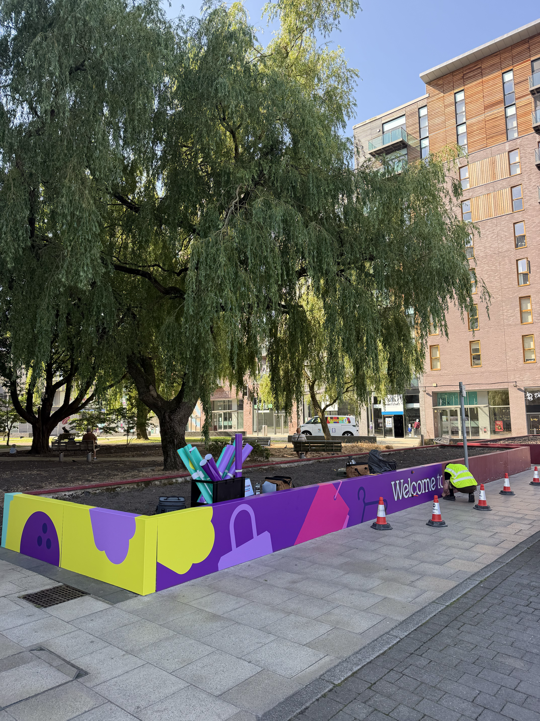 Colourful printed planter wrap reading Welcome to, installed at The Rock shopping district in Bury